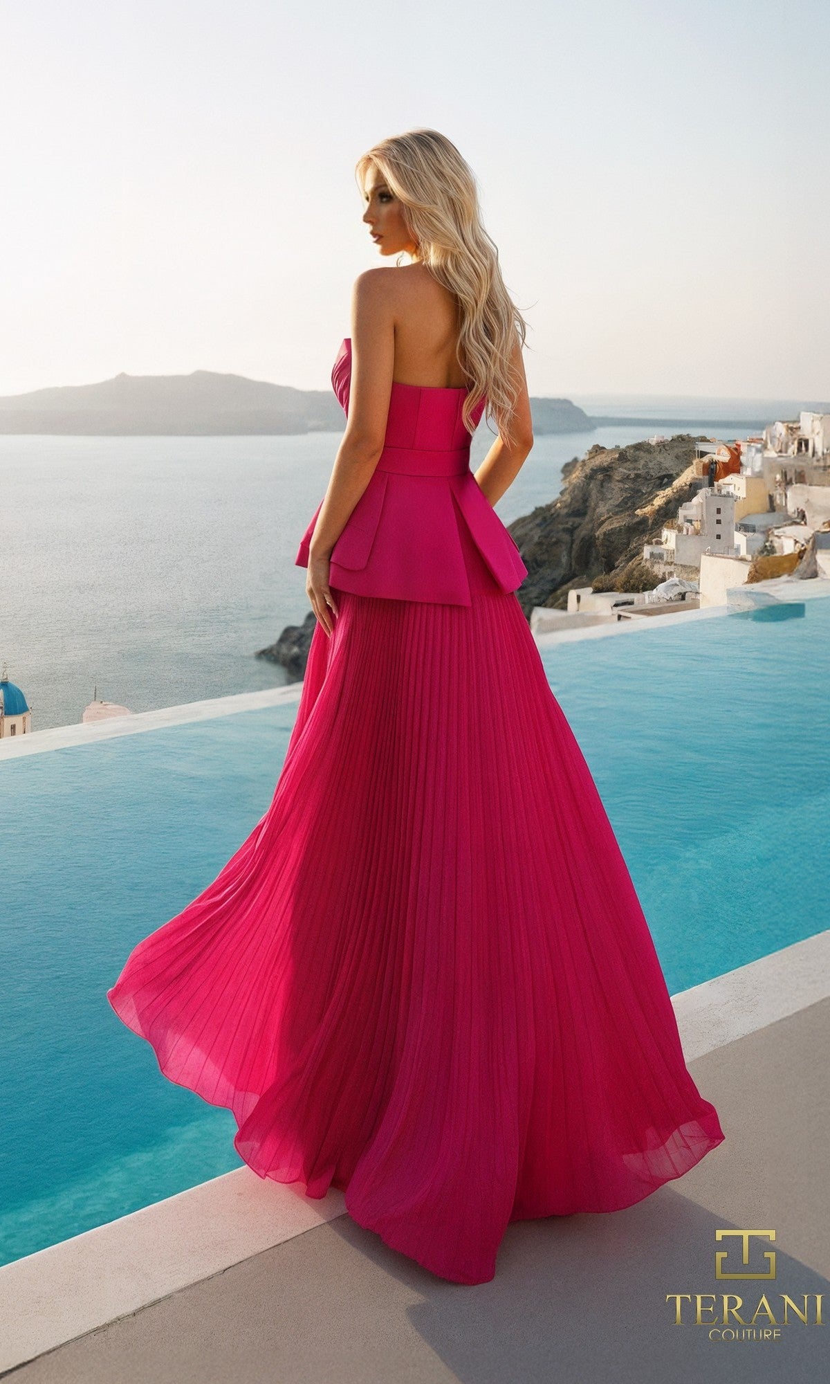 A woman in the Terani 261E6755 long formal dress stands by an infinity pool overlooking the sea and white hillside buildings, her bright pink pleated chiffon gown flowing elegantly.